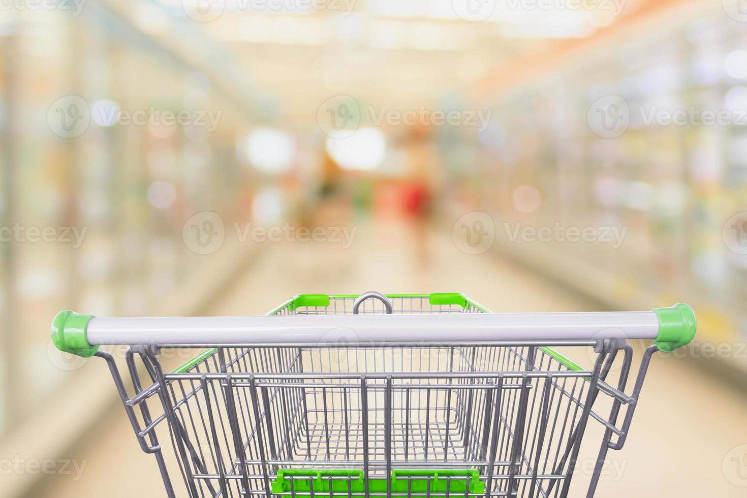 vista do carrinho de compras com borrão abstrato do corredor do supermercado congelados e produtos lácteos no fundo das prateleiras da geladeira foto
