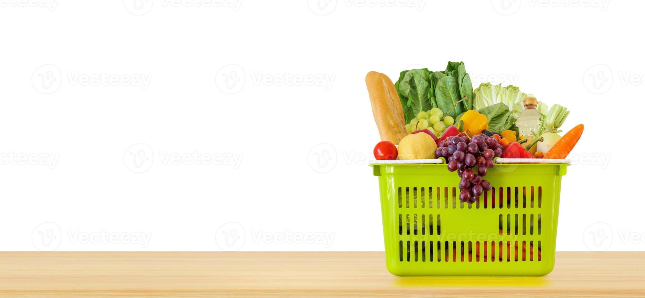 produto de mercearia de frutas e legumes frescas na cesta de compras verde no tampo da mesa de madeira isolado no fundo branco foto