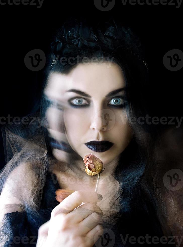 mulher gótica de cabelo escuro com maquiagem de lábios pretos e rosa seca na mão foto