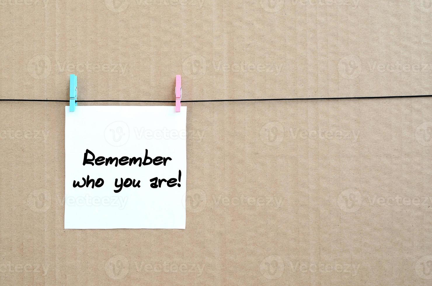 lembre-se de quem você é a nota está escrita em um adesivo branco pendurado com um prendedor de roupa em uma corda em um fundo de papelão marrom foto