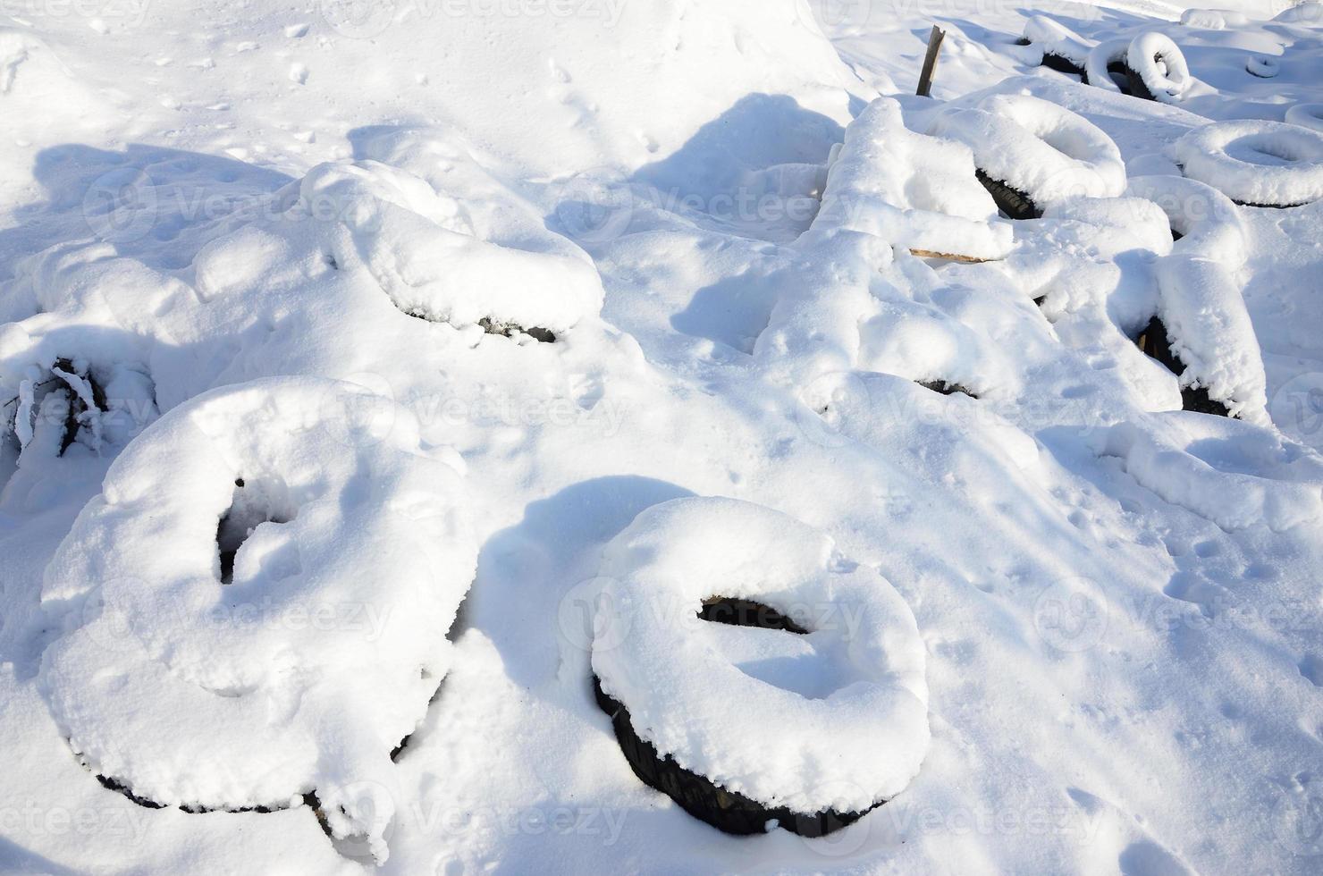 pneus de carros usados e descartados ficam na beira da estrada, cobertos com uma espessa camada de neve foto