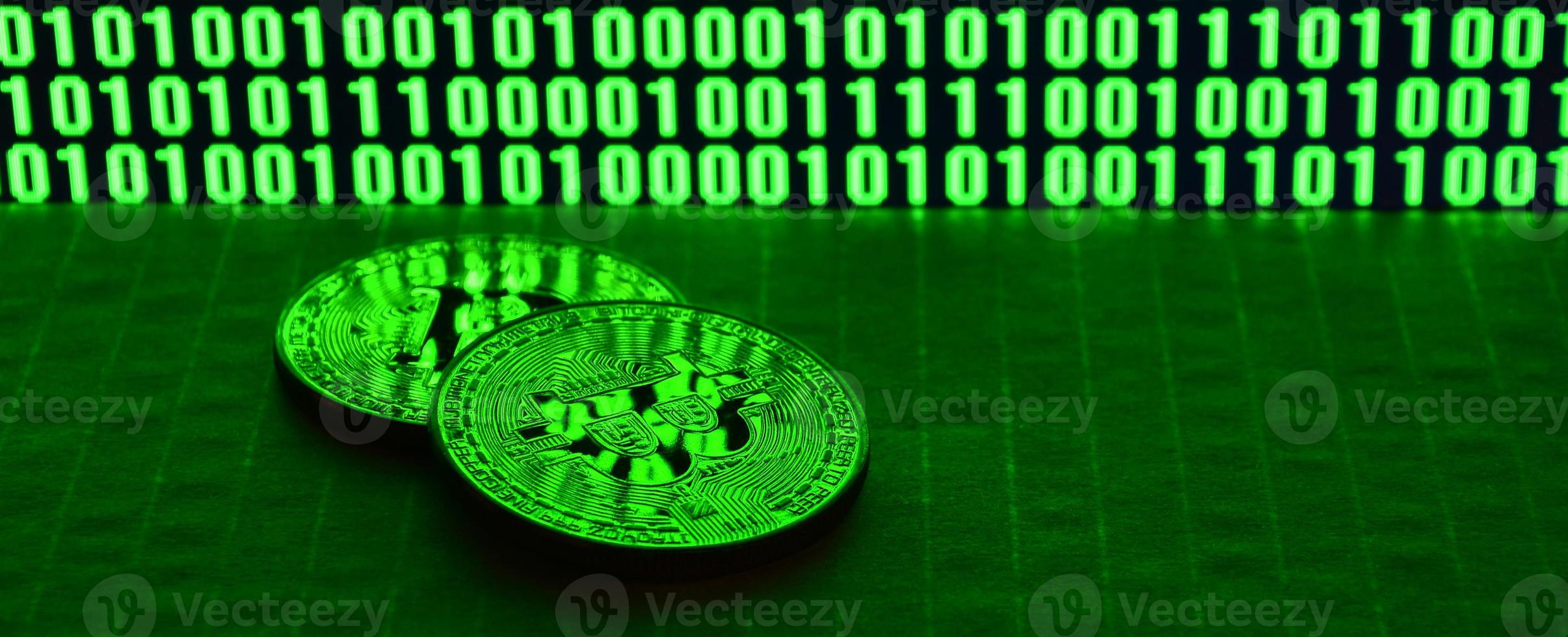 um par de bitcoins está em uma superfície de papelão no fundo de um monitor representando um código binário de zeros verdes brilhantes e unidades de um em um fundo preto. iluminação baixa chave foto