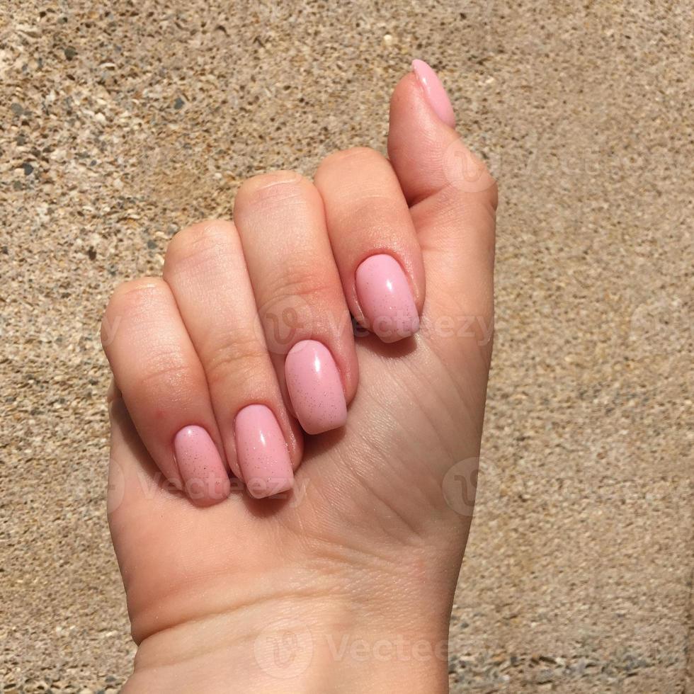 mãos femininas com manicure rosa elegante em fundo marrom foto