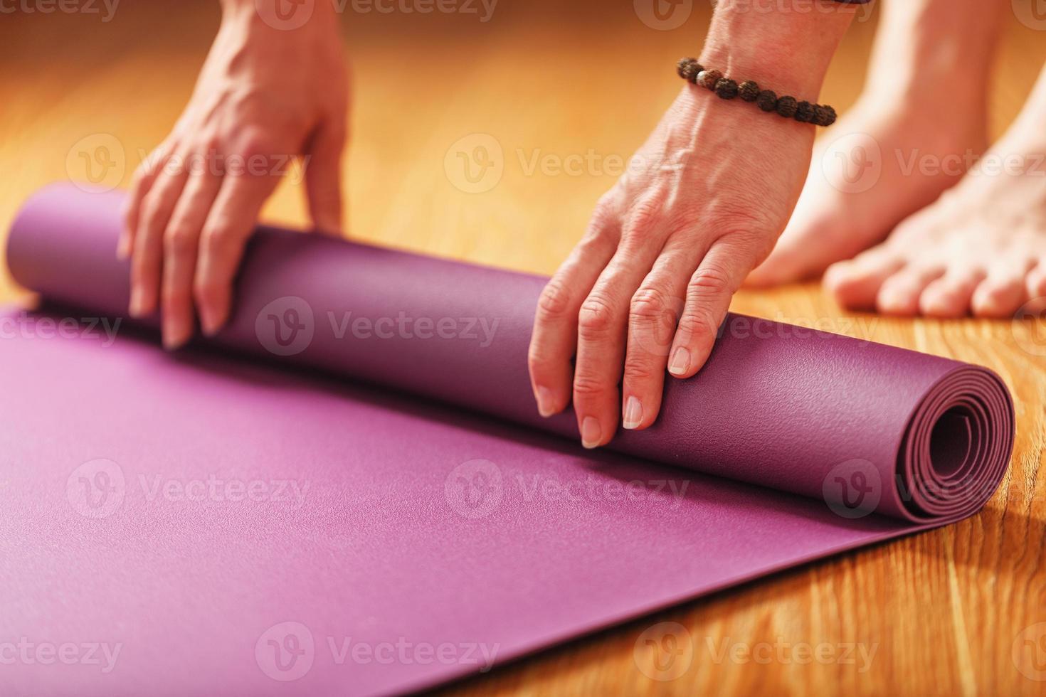 as mãos de uma mulher colocam um tapete de ioga ou fitness lilás antes de uma prática de treino em casa em um piso de madeira. foto