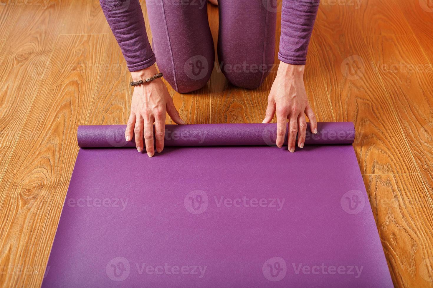 uma mulher coloca um tapete de ioga lilás no chão de madeira. foto