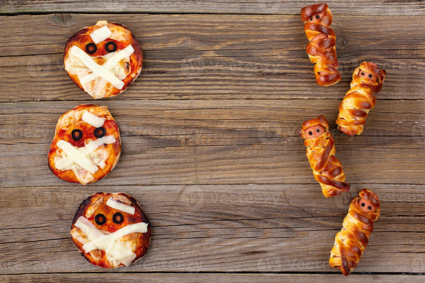 mini pizza como múmias e múmias de salsicha assustadoras em massa para crianças. comida louca e engraçada de halloween para crianças foto