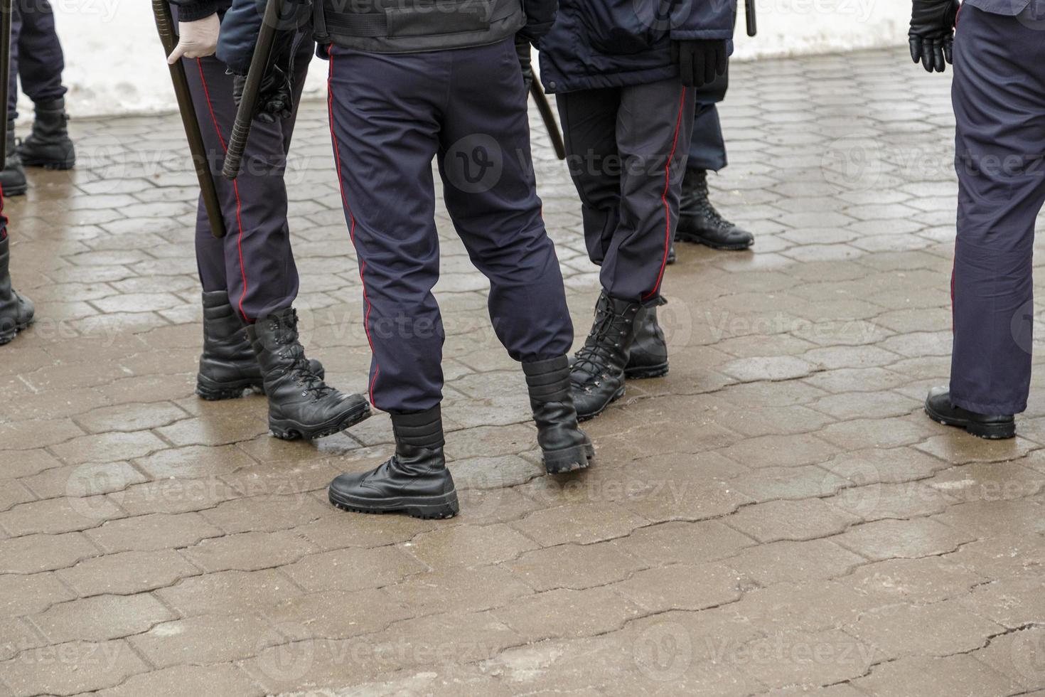 Pernas de policiais russos em botas pretas, calças listradas vermelhas e com bastões de noite de tonfa de borracha. foto