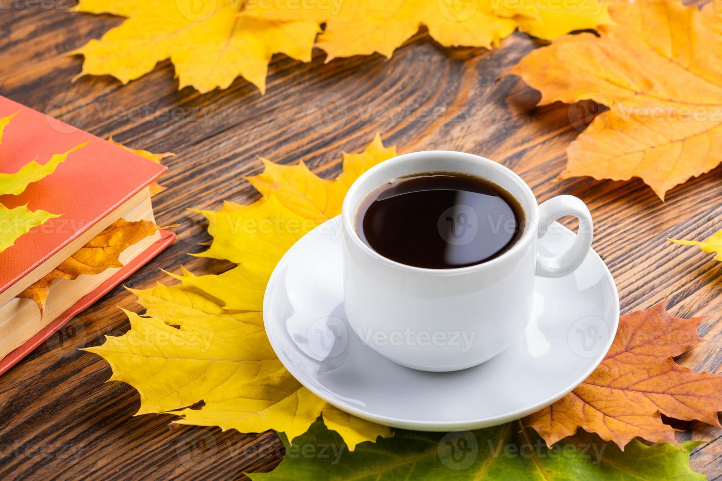 xícara de café branco clássico na mesa de madeira com livro e folhas de bordo outonais coloridas foto