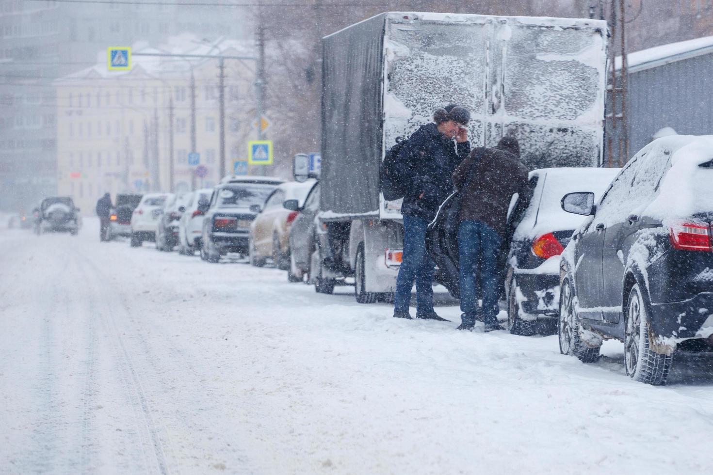 tula, rússia, 13 de fevereiro de 2020, dois homens parados perto do carro estacionado ao lado da estrada da cidade durante uma forte tempestade de neve à luz do dia foto