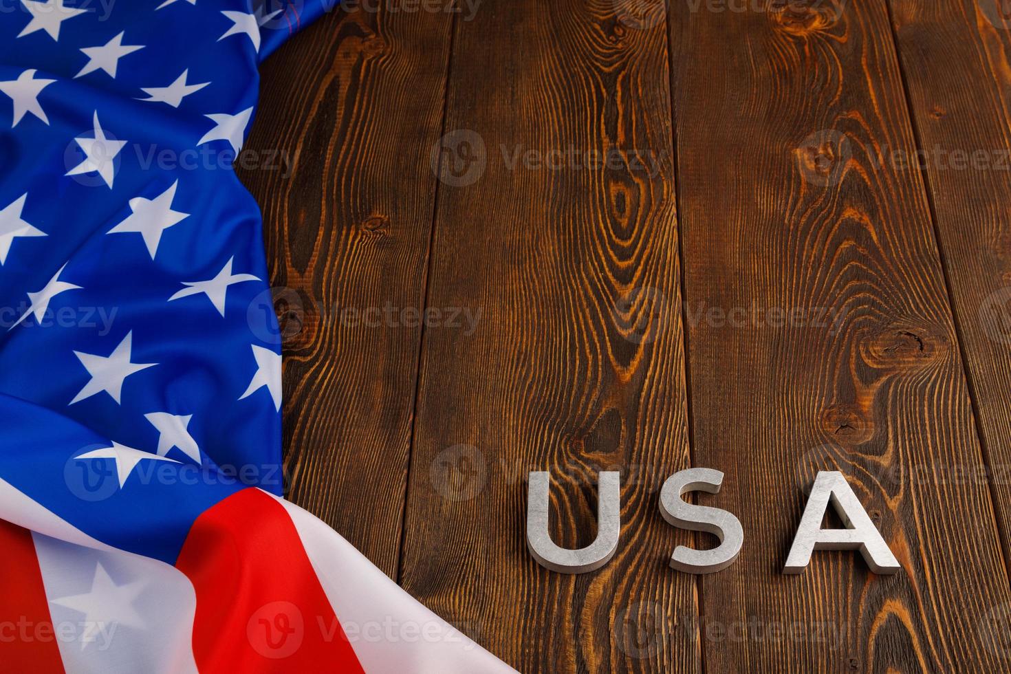 a palavra eua colocada com letras de metal prateado na superfície da placa de madeira sob a bandeira amassada dos estados unidos da américa foto