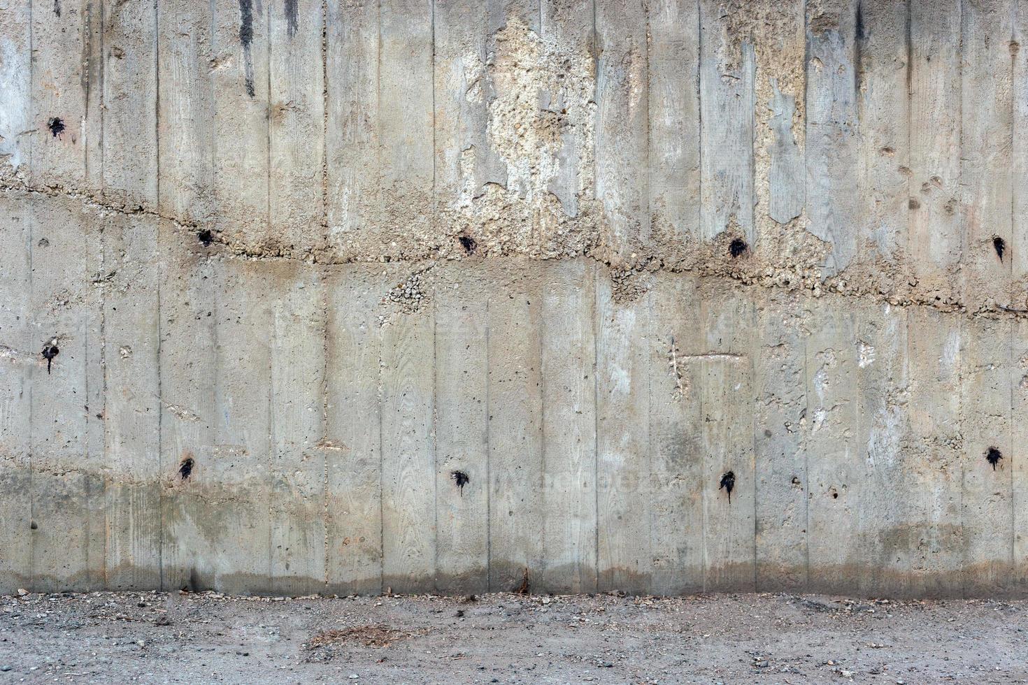 uma parede de concreto cinza áspera grossa ao ar livre com parte da superfície do piso, impressões visíveis de pranchas de madeira foto