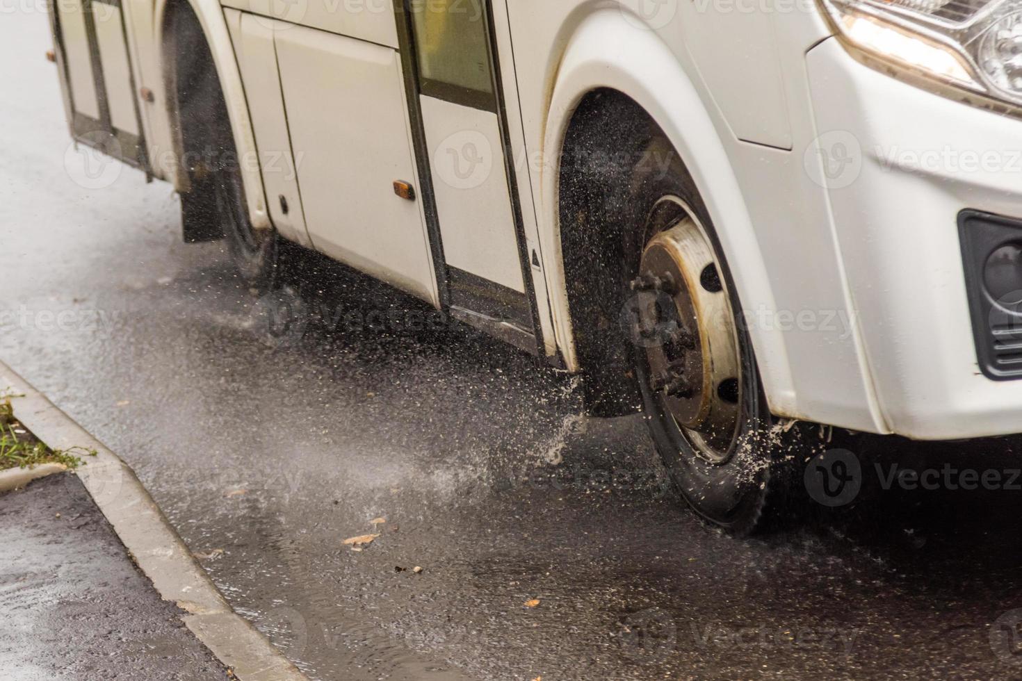 ônibus municipal branco movendo-se na estrada chuvosa com salpicos de água foto