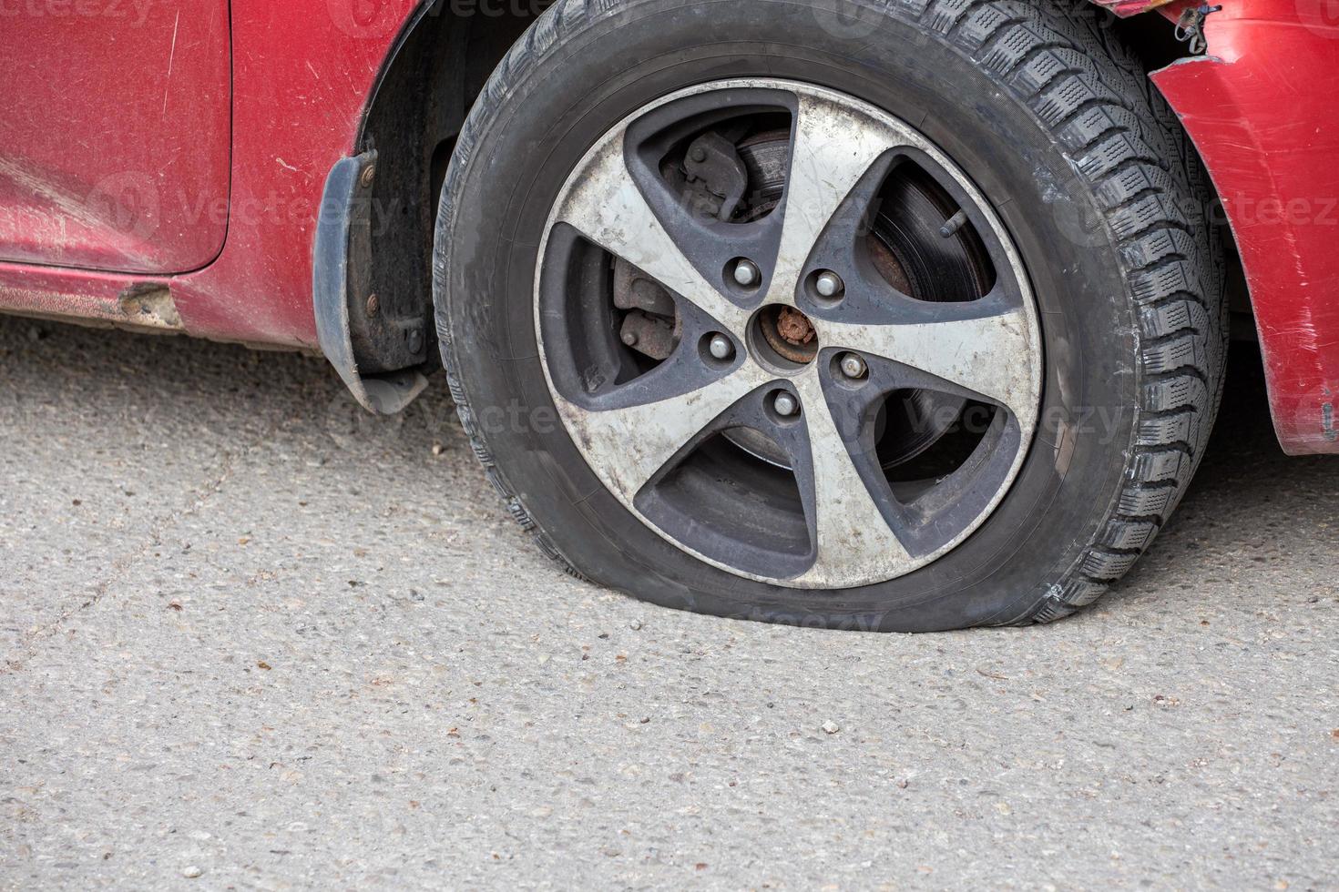 close-up de pneu furado de carro civil vermelho velho em dia ensolarado seco na superfície de asfalto cinza foto