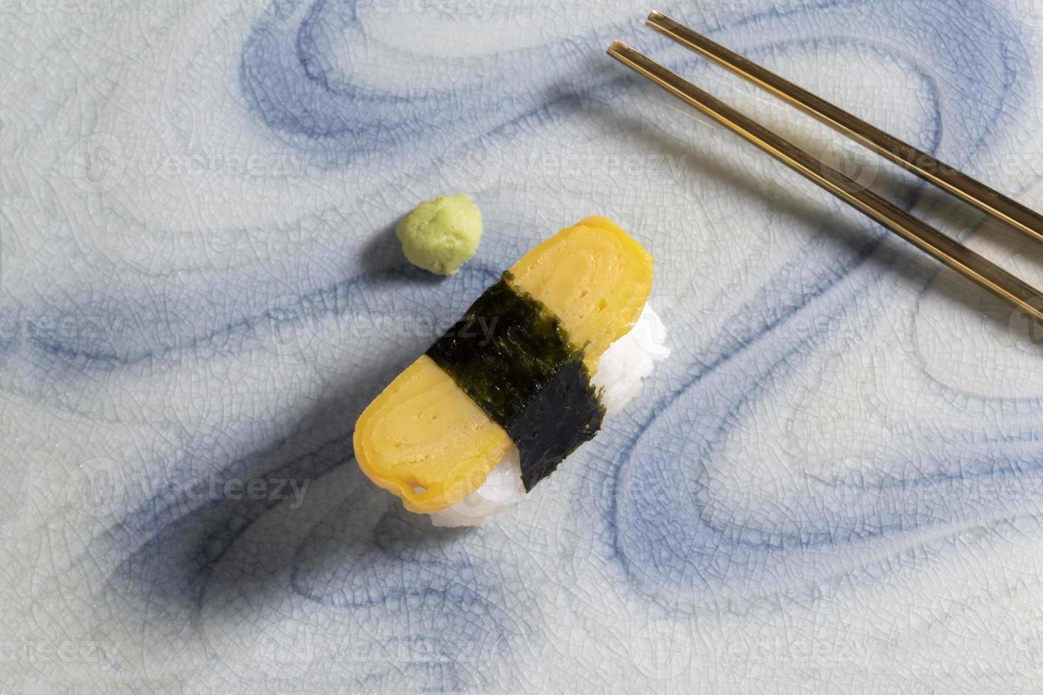 sushi de tamagoyaki de comida japonesa no prato tem pauzinhos no fundo. foto