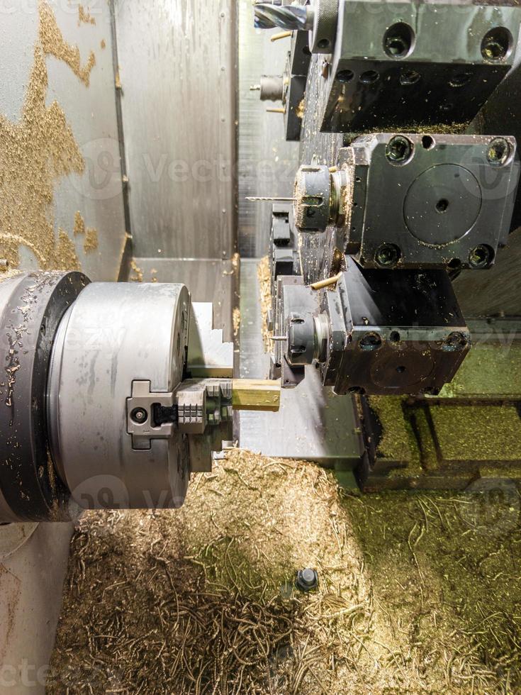 torno cnc com muita limalha de latão dentro enquanto gira a peça de trabalho de haste de metal amarelo hexagonal foto