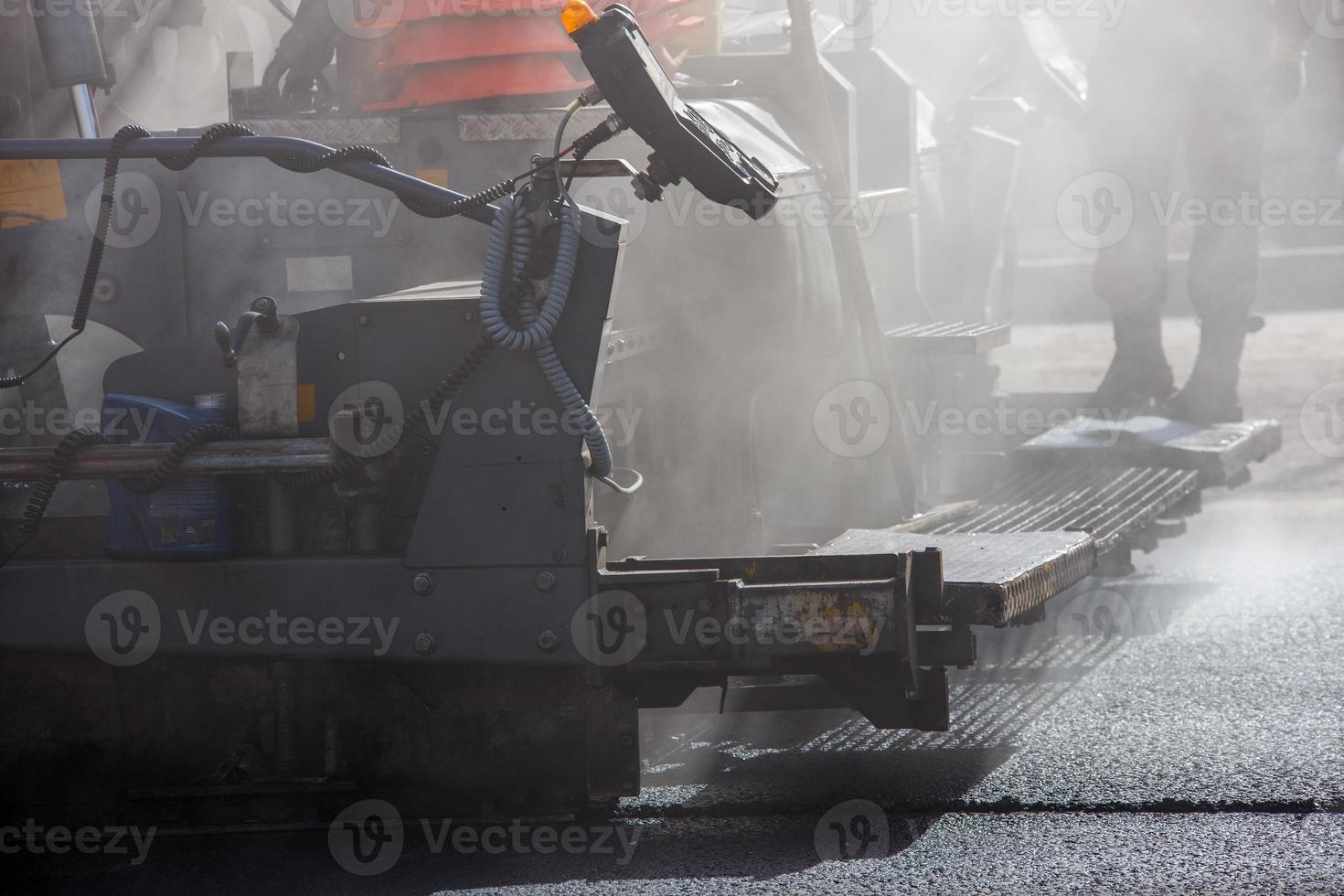 Vista aproximada da máquina de pavimentação de asfalto durante trabalhos de reparação de estradas à luz do dia com fumaça e vapor no ar foto