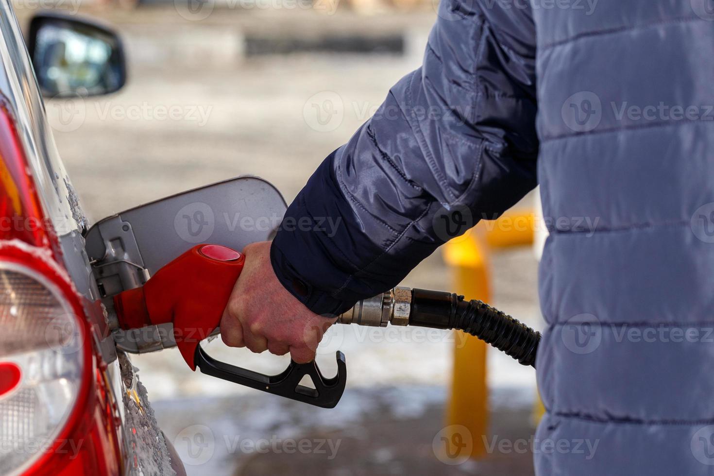 mão de velho no casaco azul quente reabastecendo carro metálico cinza no posto de gasolina durante o dia - close-up com foco seletivo foto