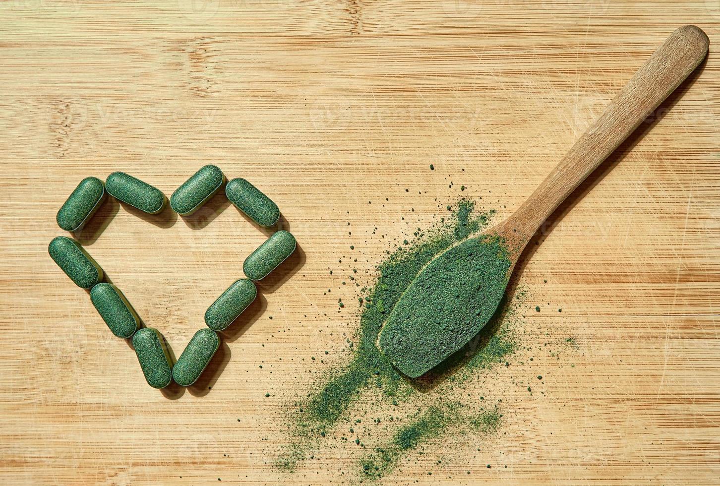 comprimidos de chlorella ou spirulina e pó em uma colher de pau sobre um fundo claro de madeira. suplemento nutricional, superalimento detox foto