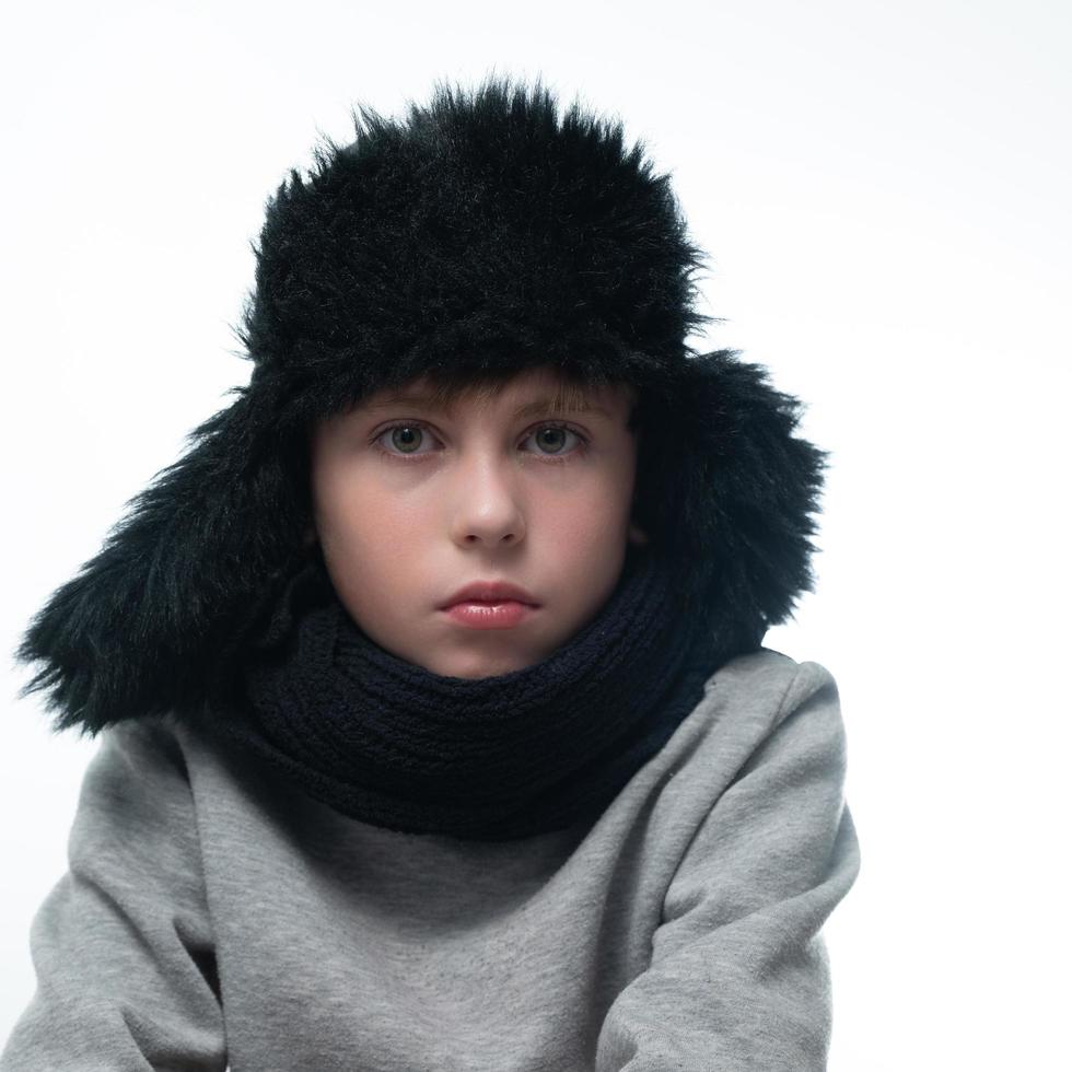 retrato de uma criança com um chapéu de inverno com protetores de ouvido e um cachecol de malha em um fundo branco. foto
