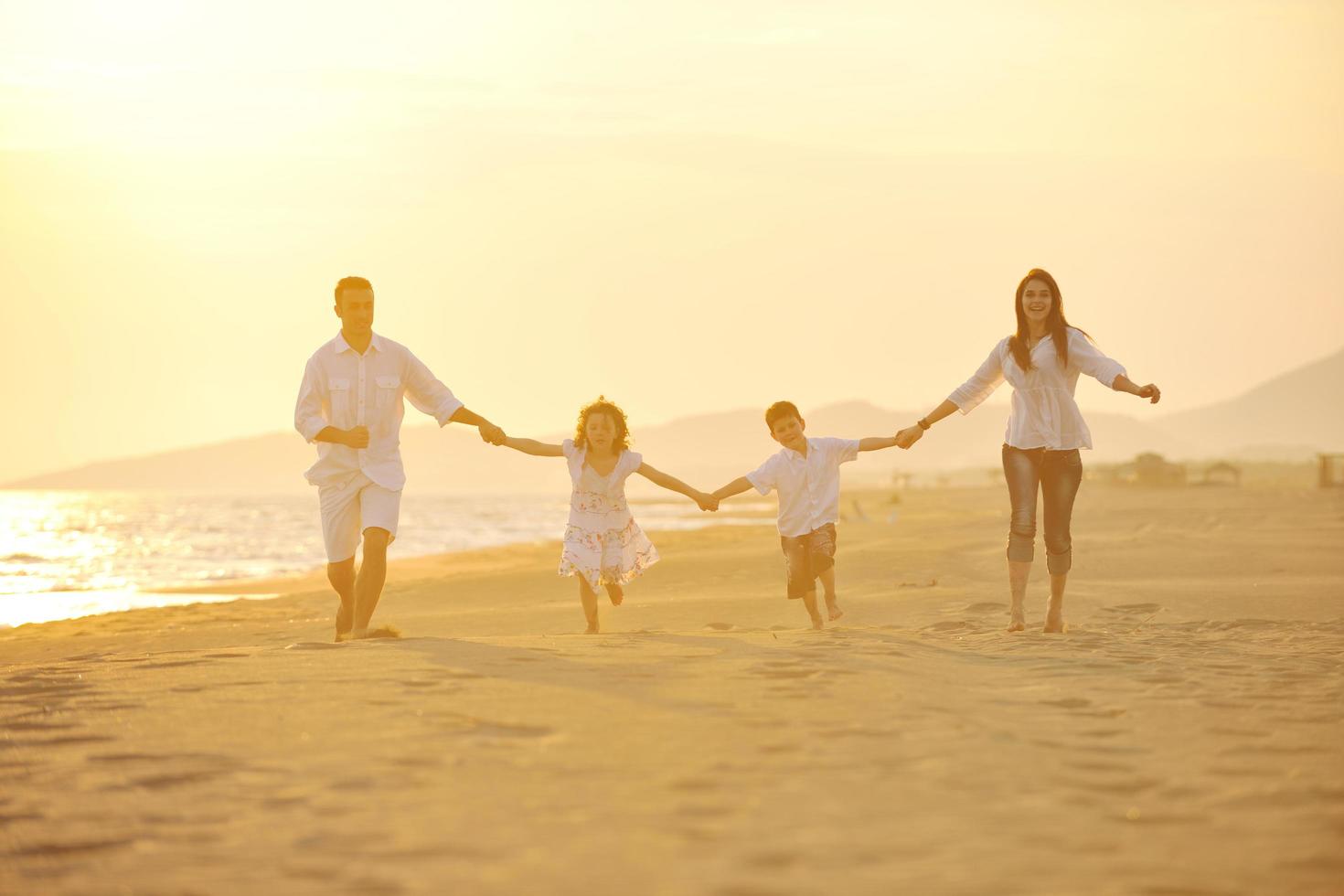 família jovem feliz se diverte na praia ao pôr do sol foto