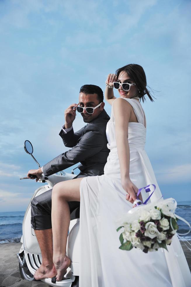 casal recém casado na praia anda de scooter branca foto