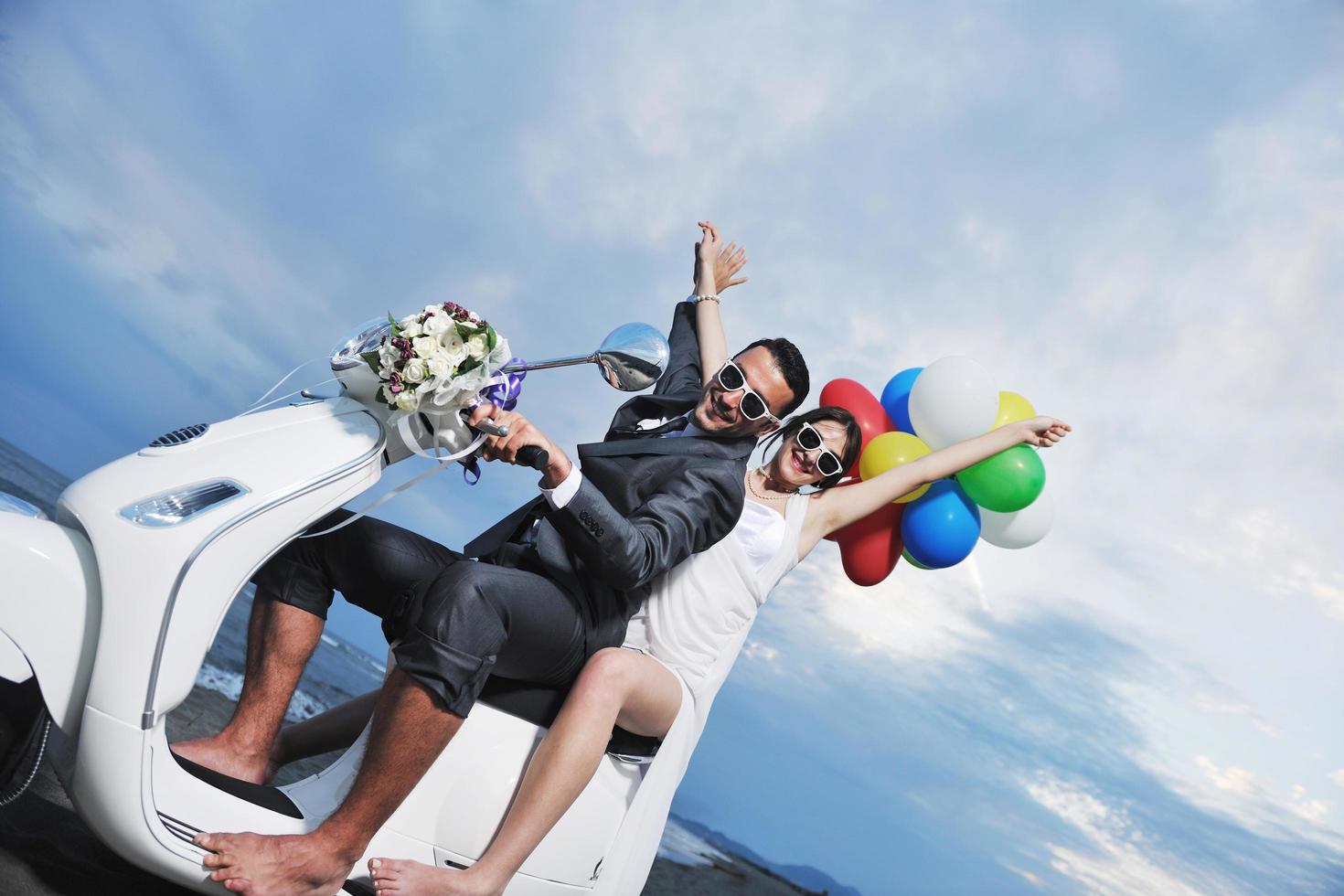 casal recém casado na praia anda de scooter branca foto