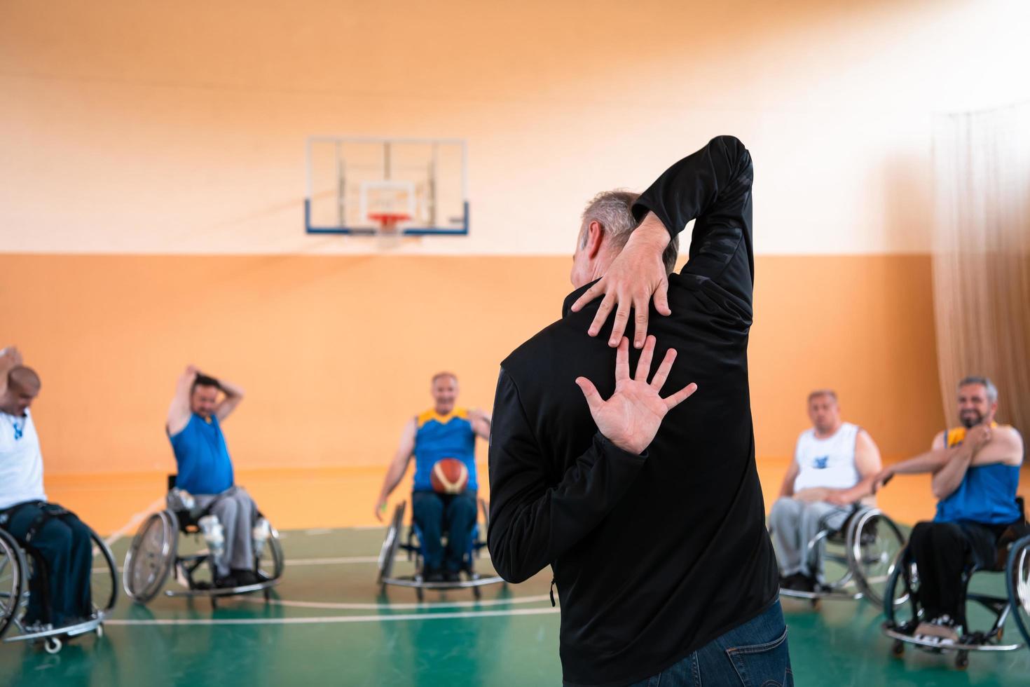 o selecionador do time de basquete com deficiência fica na frente dos jogadores e mostra os exercícios de alongamento antes do início do treinamento foto