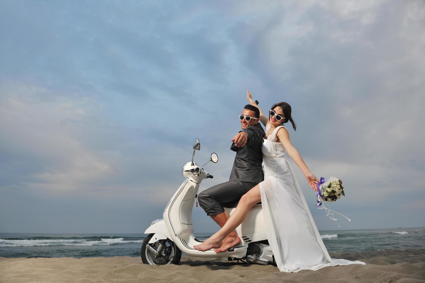 casal recém casado na praia anda de scooter branca foto