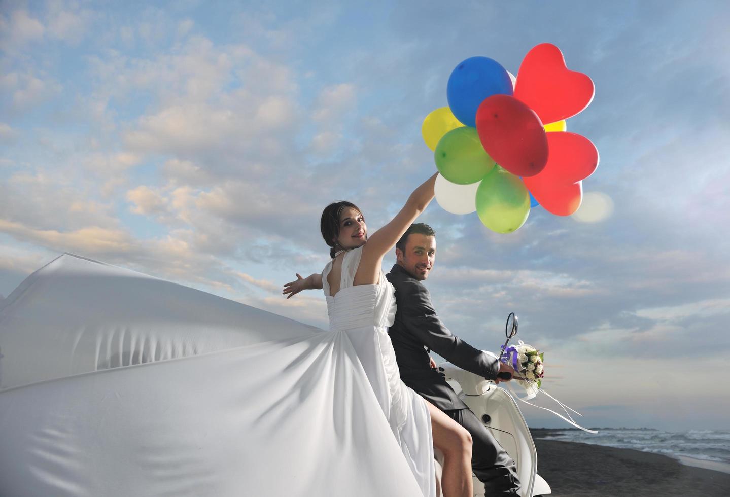 casal recém casado na praia anda de scooter branca foto