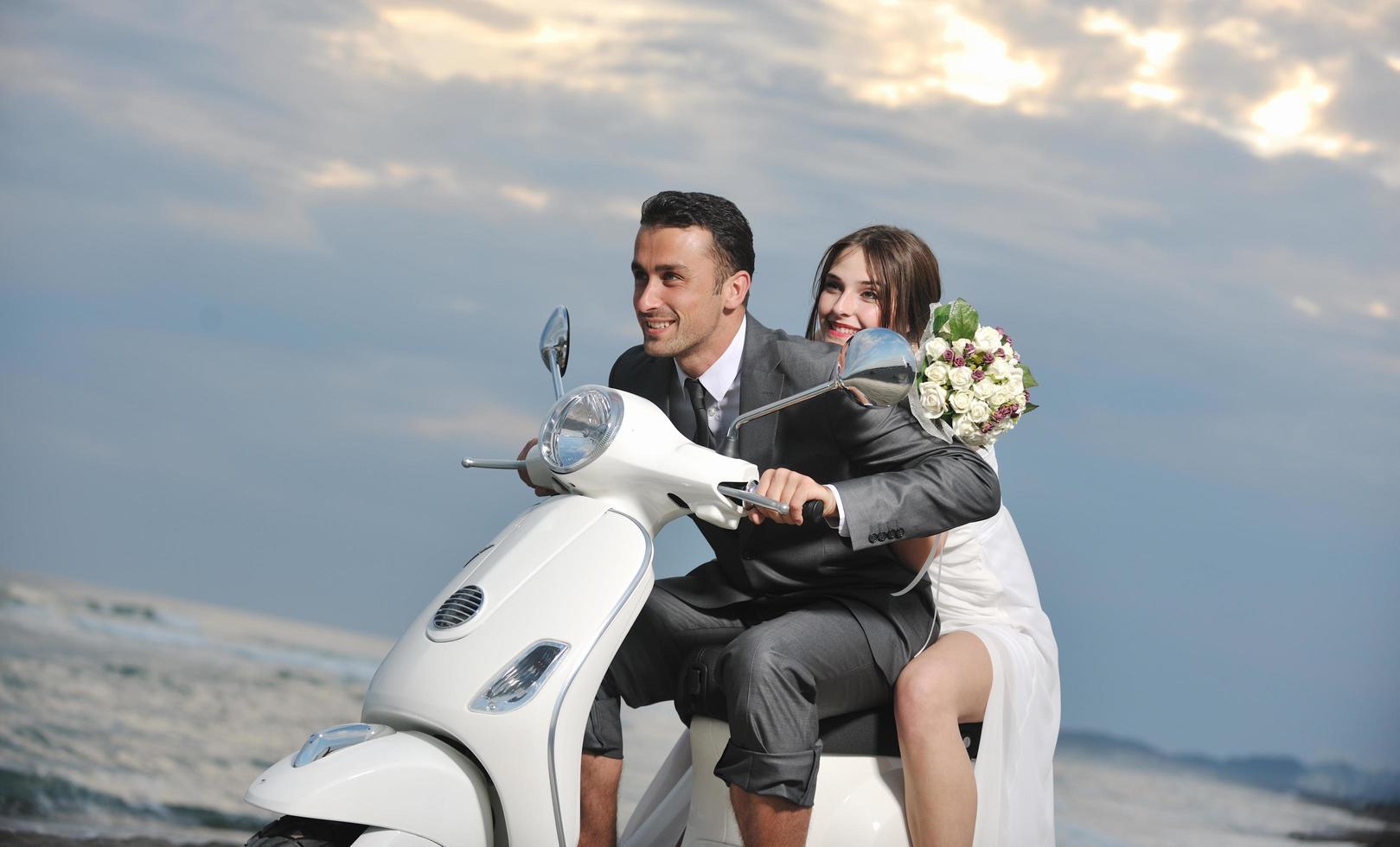 casal recém casado na praia anda de scooter branca foto