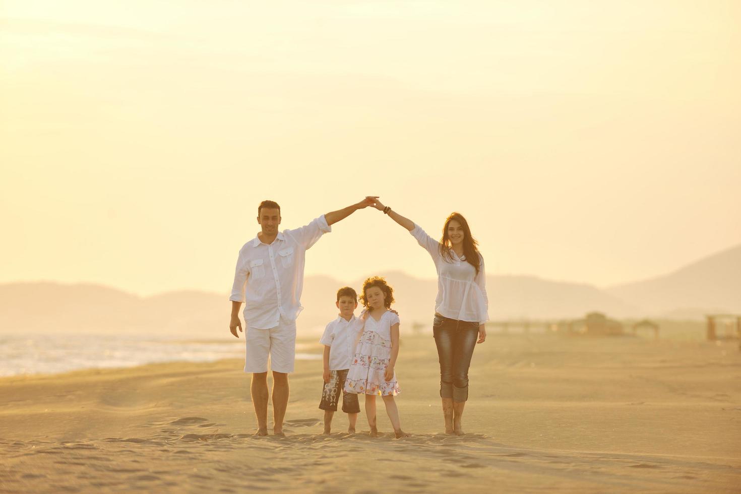 família jovem feliz se diverte na praia ao pôr do sol foto