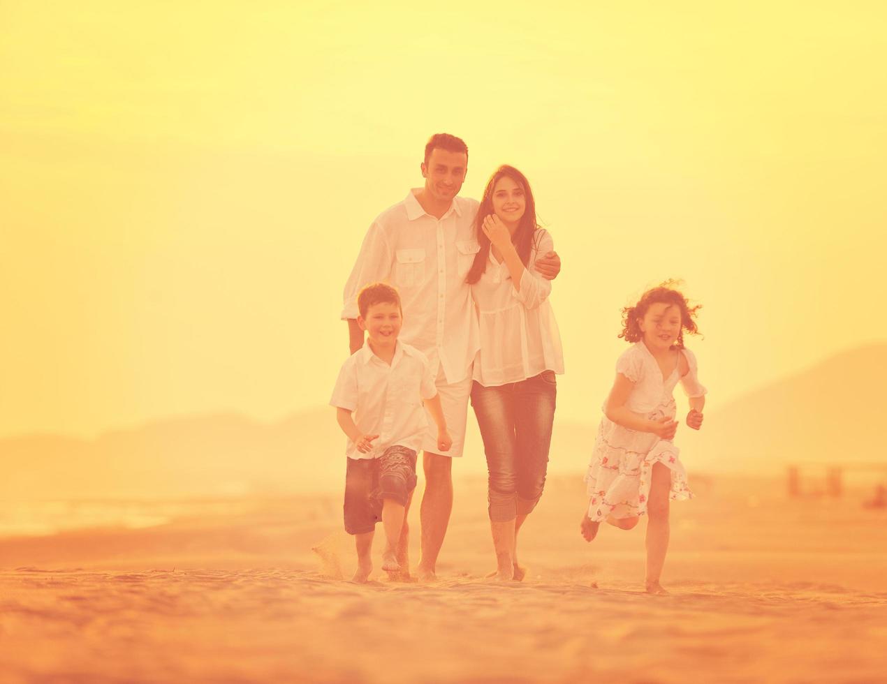 família jovem feliz se diverte na praia ao pôr do sol foto