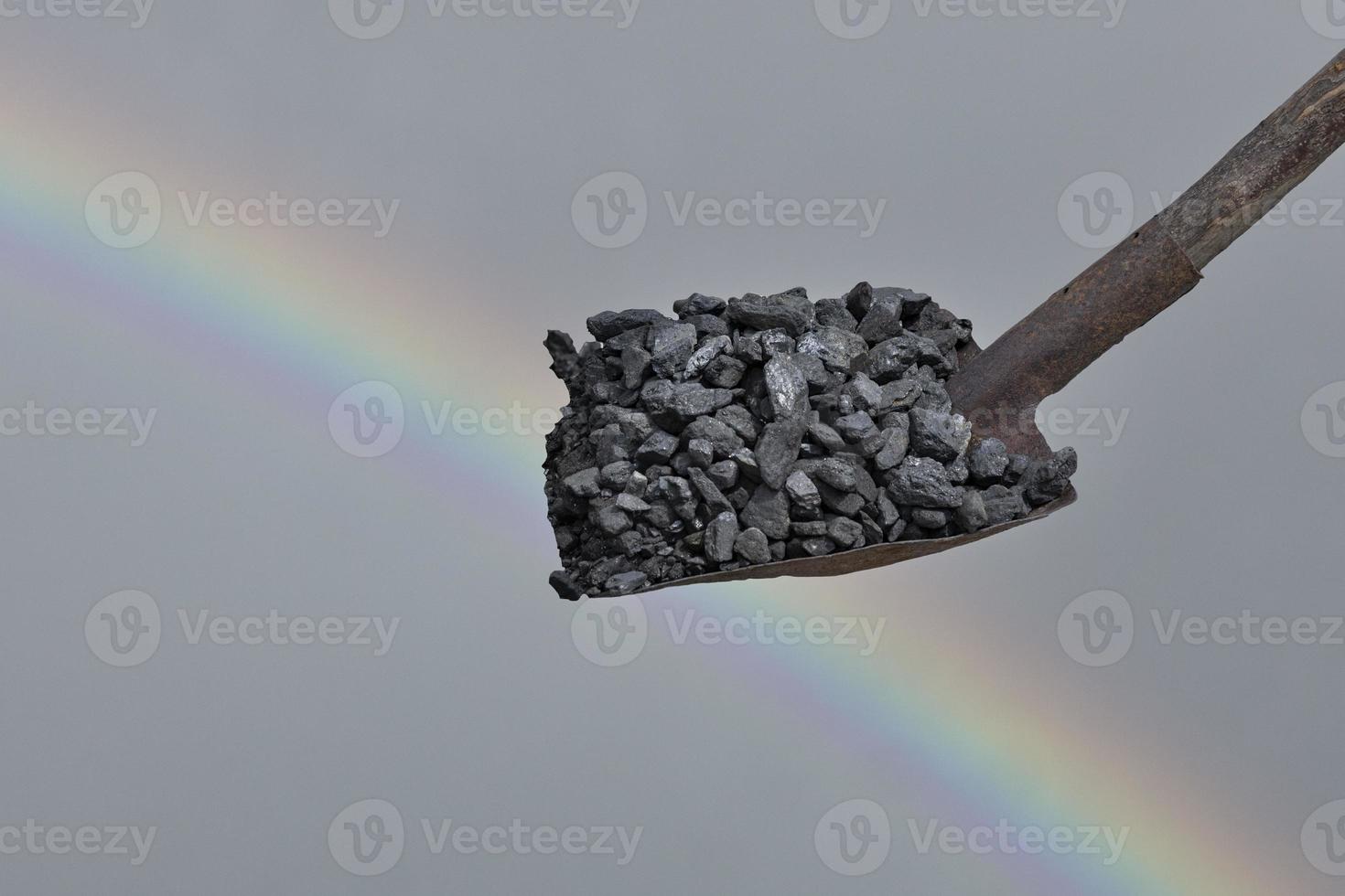 carvão preto em uma pá contra o céu e um arco-íris. crise de energia. foto