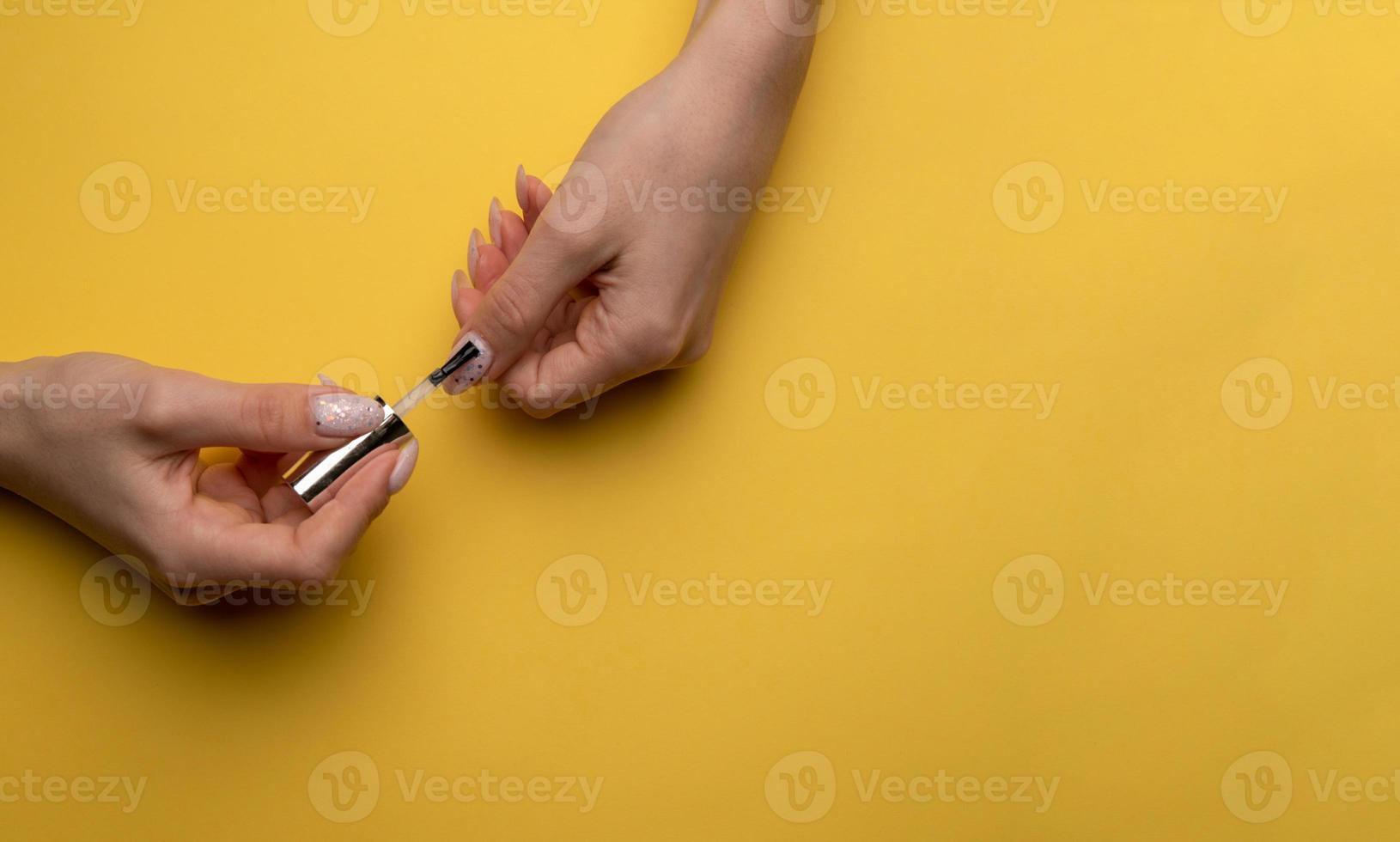 close-up de uma mulher pinta as unhas com laca em um fundo amarelo, vista superior foto