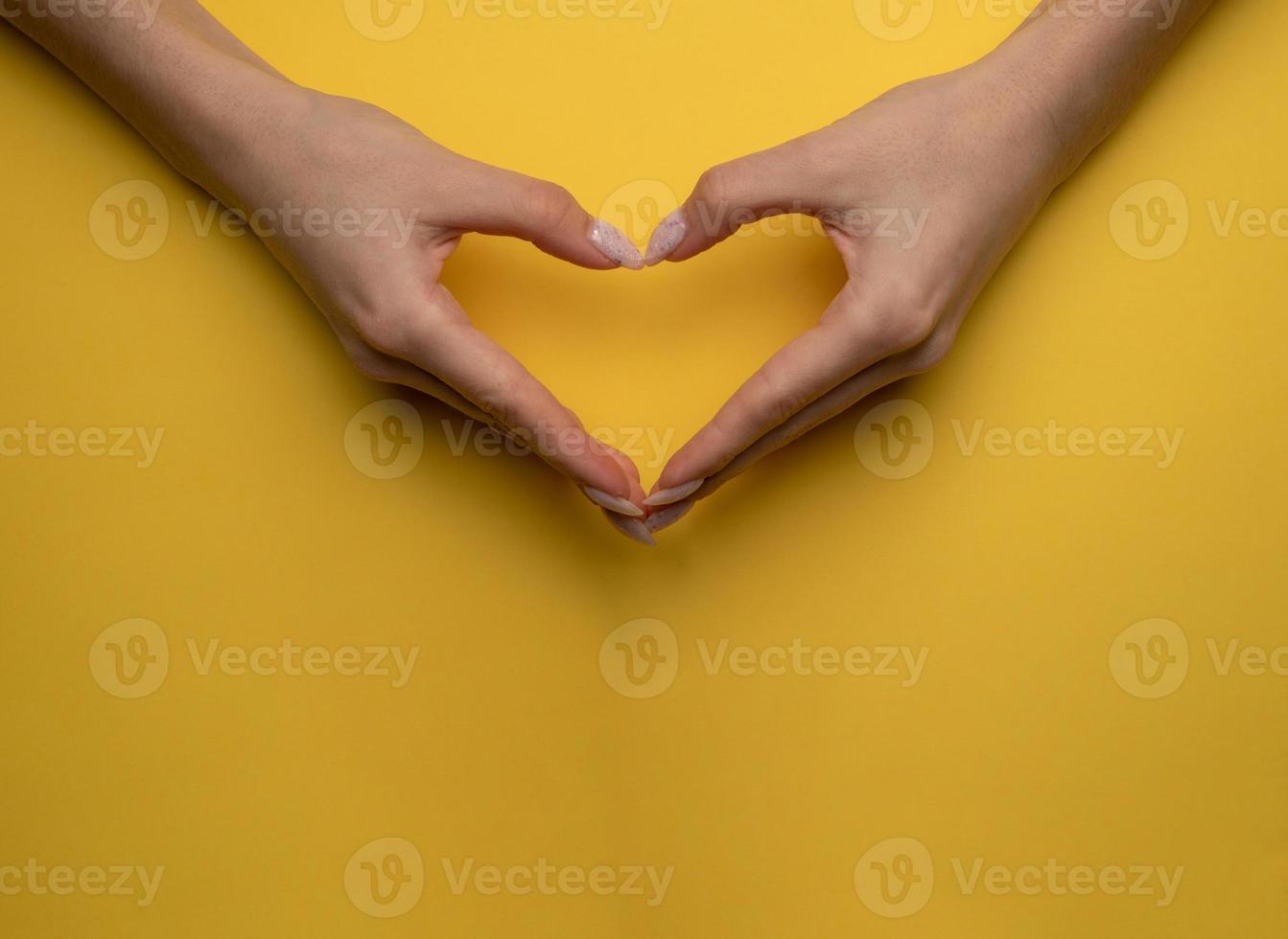 coração fazendo as mãos da mulher com manicure em fundo amarelo, vista superior foto