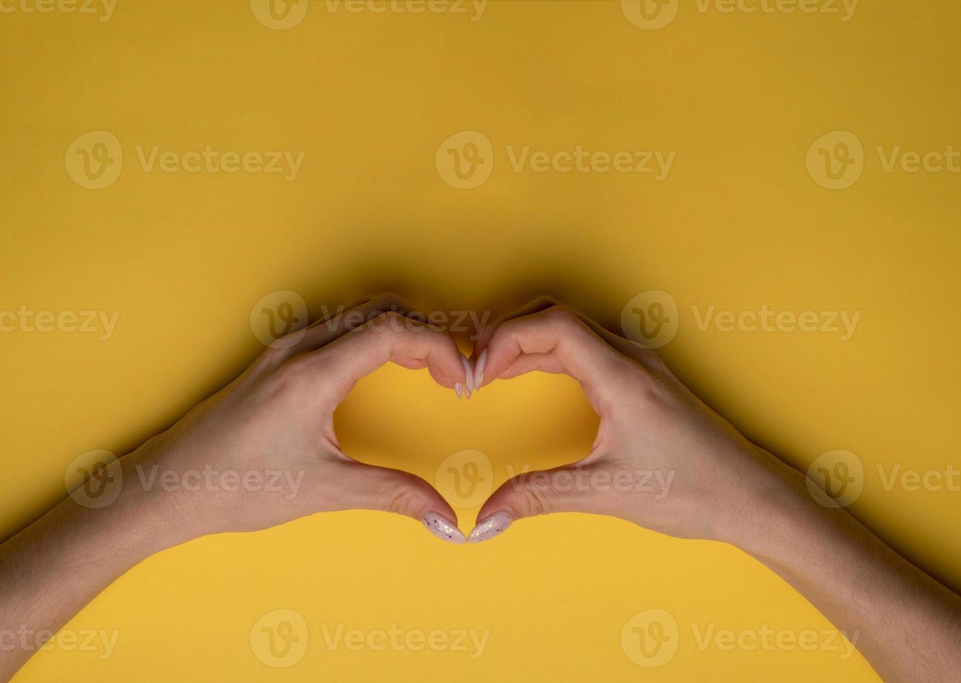 coração fazendo as mãos da mulher com manicure em fundo amarelo, vista superior foto