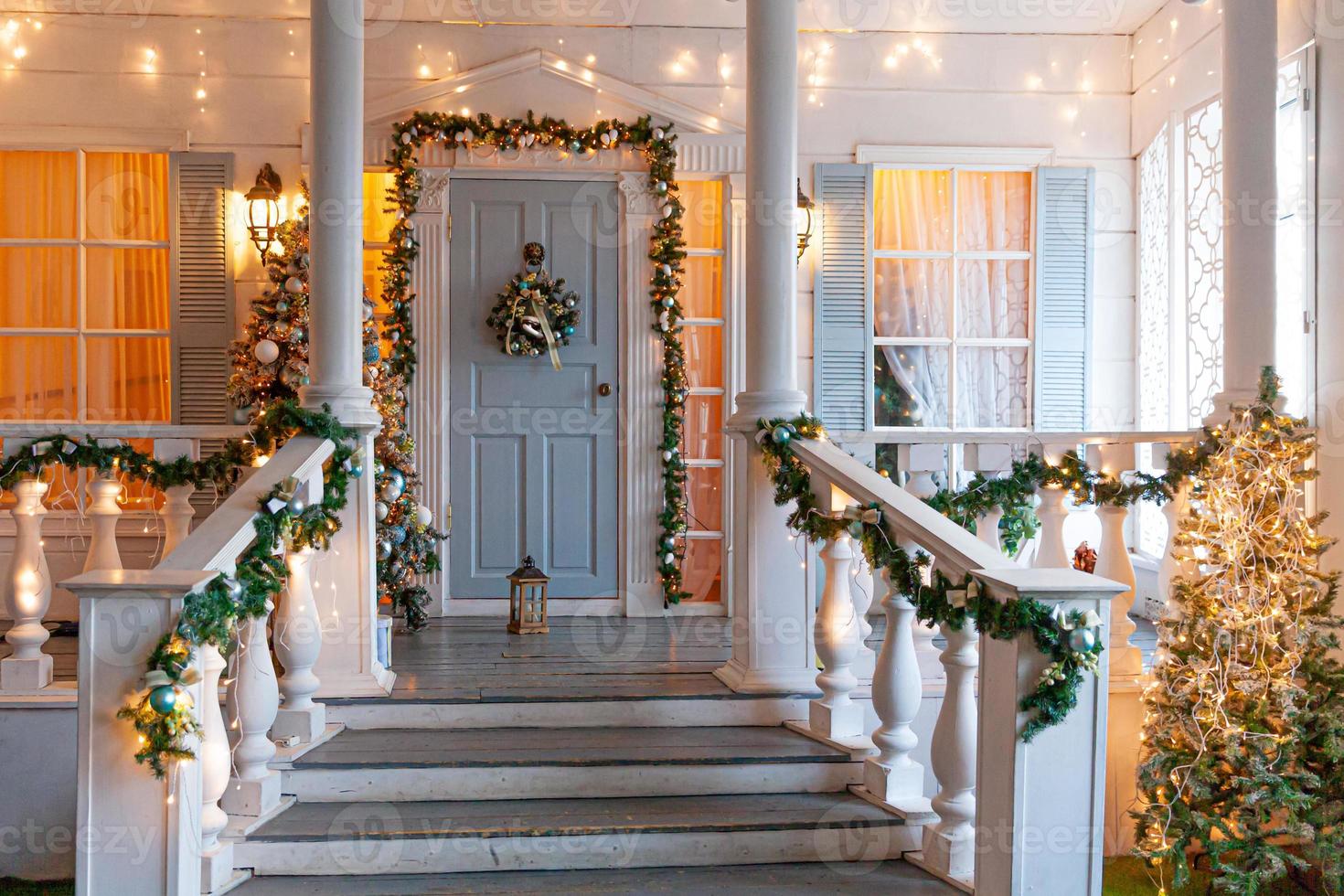 ideia de decoração de varanda de natal. entrada da casa decorada para férias. guirlanda de grinalda dourada e verde de galhos de árvores do abeto e luzes na grade. véspera de natal em casa foto