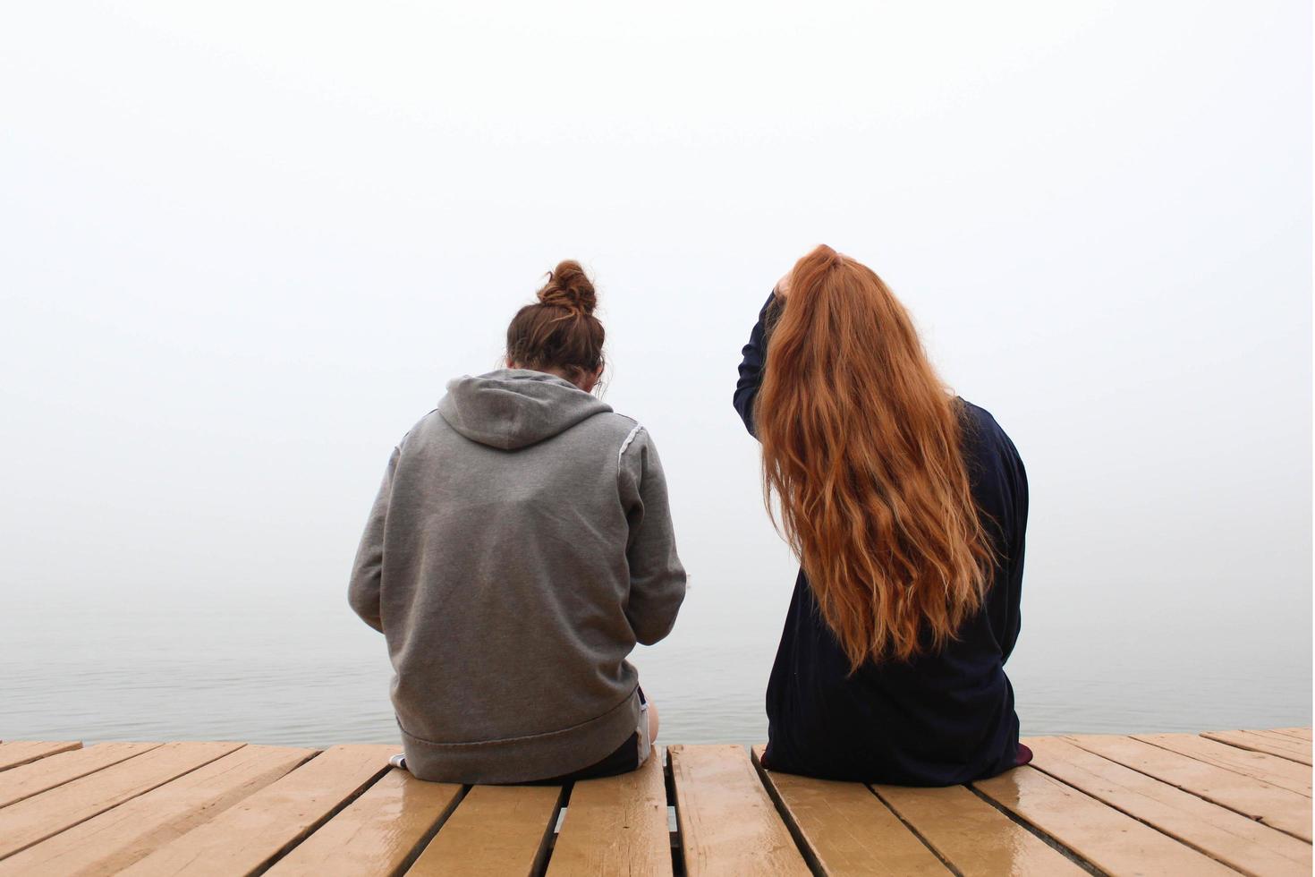 duas mulheres sentadas em um píer de madeira foto