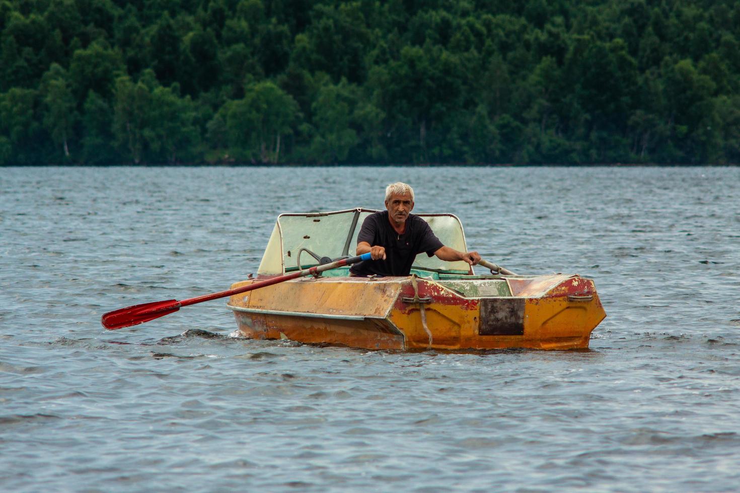 República da Carélia, Rússia - 2 de julho de 2013, velho homem bronzeado grisalho navegando no barco com remos no lago da Carélia. foto
