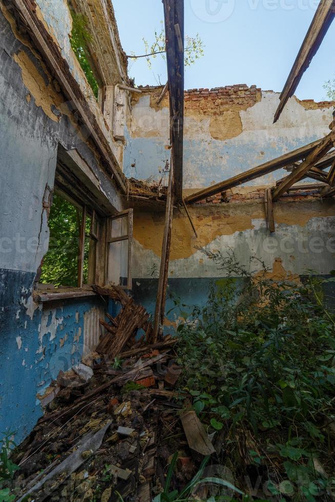 janela de madeira quebrada e sala com grama alta, vista dentro de um dormitório meio destruído abandonado à luz do dia de verão foto