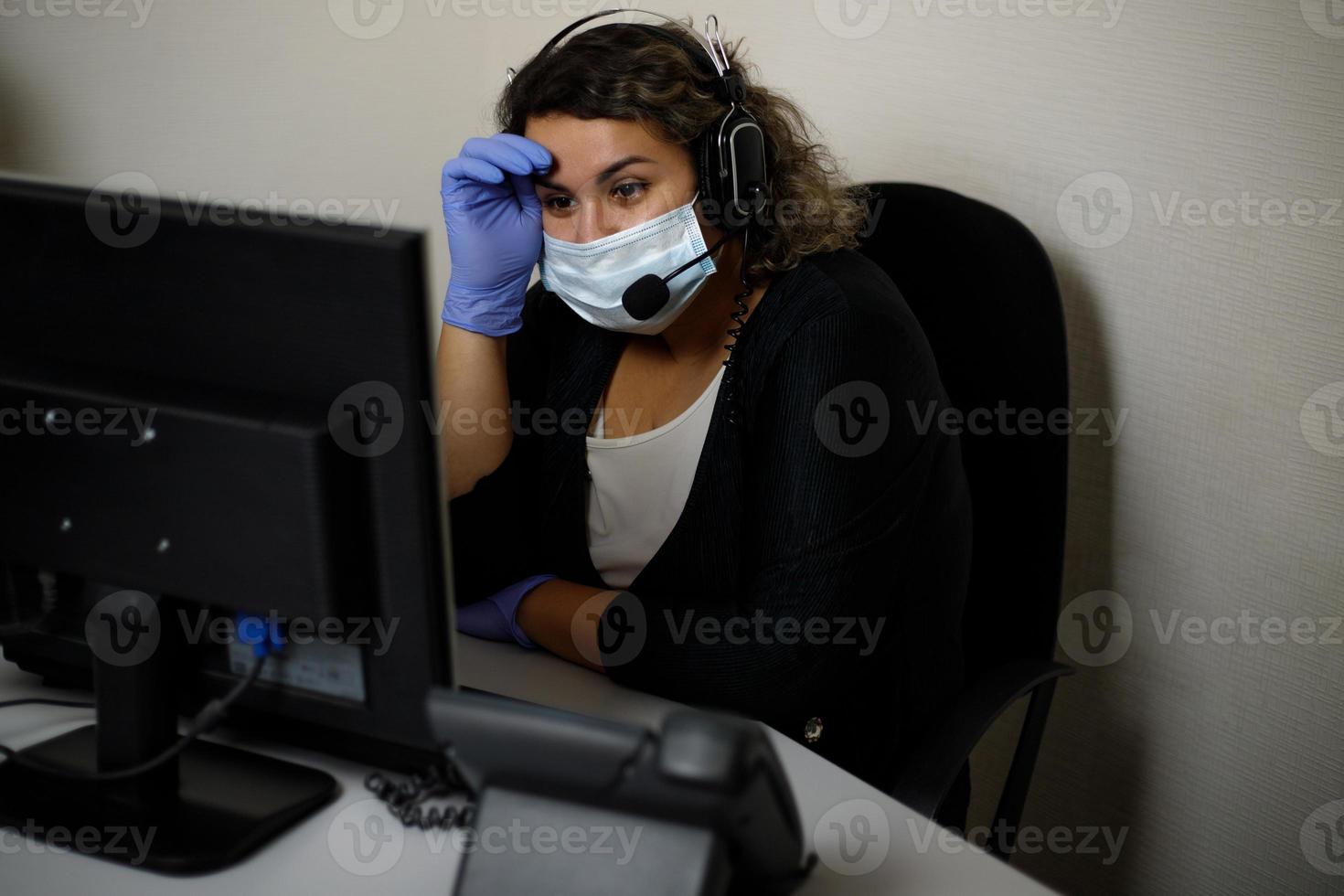 um agente de call center trabalhando na linha direta de suporte no escritório, usando máscara e luvas. o operador do call center está falando com o cliente. foto