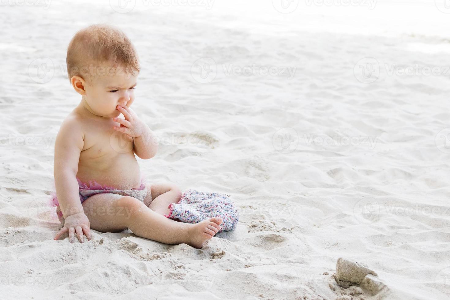 menina bonitinha de sunga rosa jogando areia na praia. desenvolvimento sensorial para crianças ao ar livre. foto