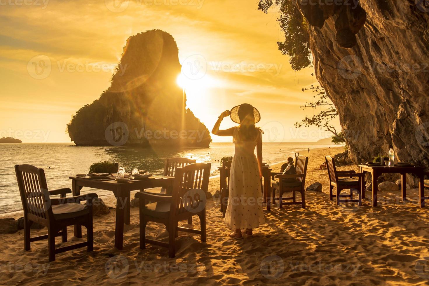 turista de mulher em jantar de vestido branco na caverna do restaurante na praia de phra nang ao pôr do sol, railay, krabi, tailândia. férias, viagens, verão, desejo de viajar e conceito de férias foto