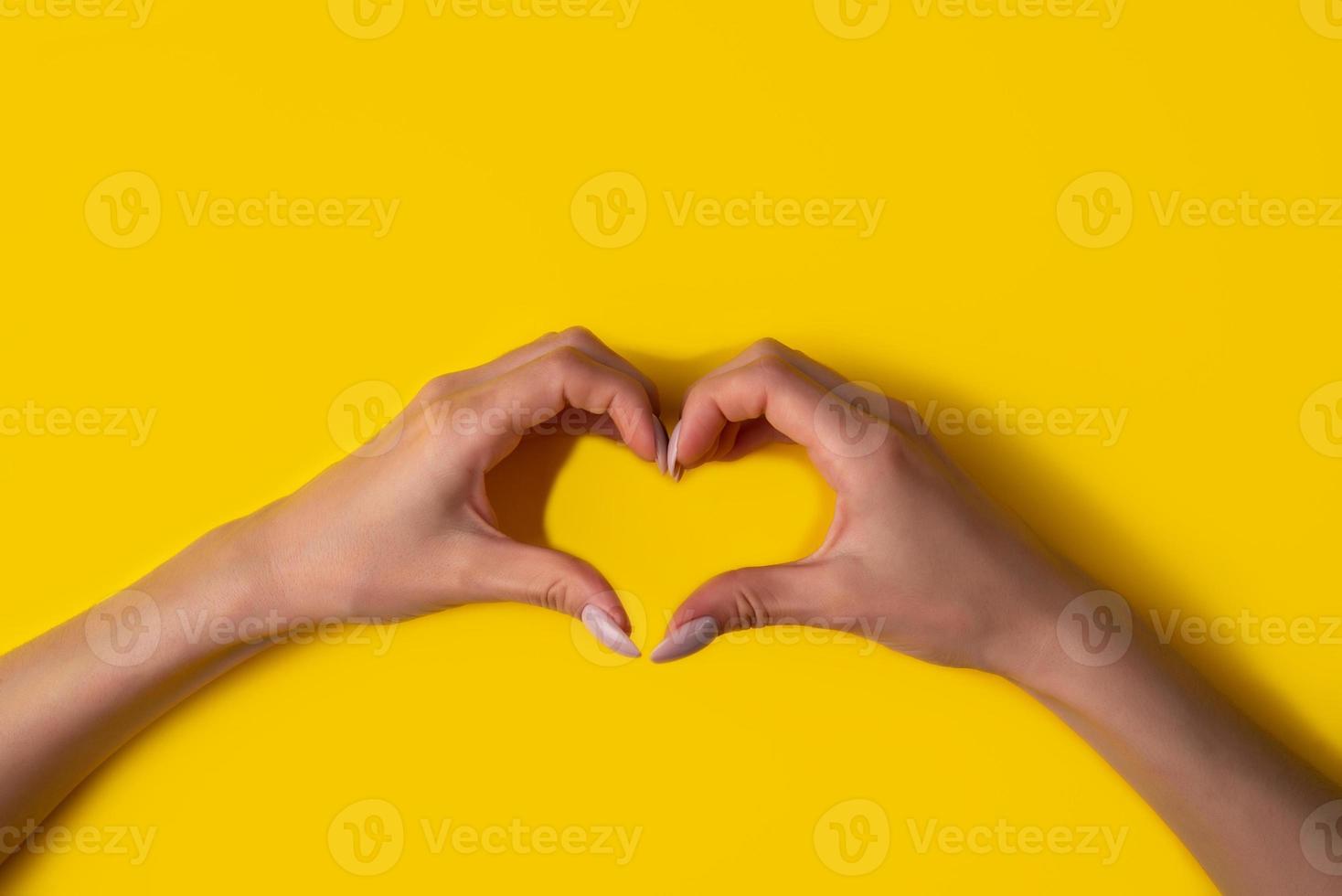 coração fazendo as mãos da mulher com manicure em fundo amarelo, vista superior foto