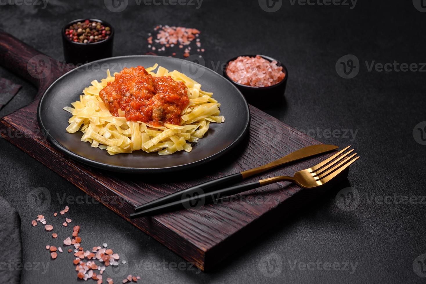 macarrão com almôndegas de carne em molho de tomate com especiarias e ervas em um fundo escuro foto