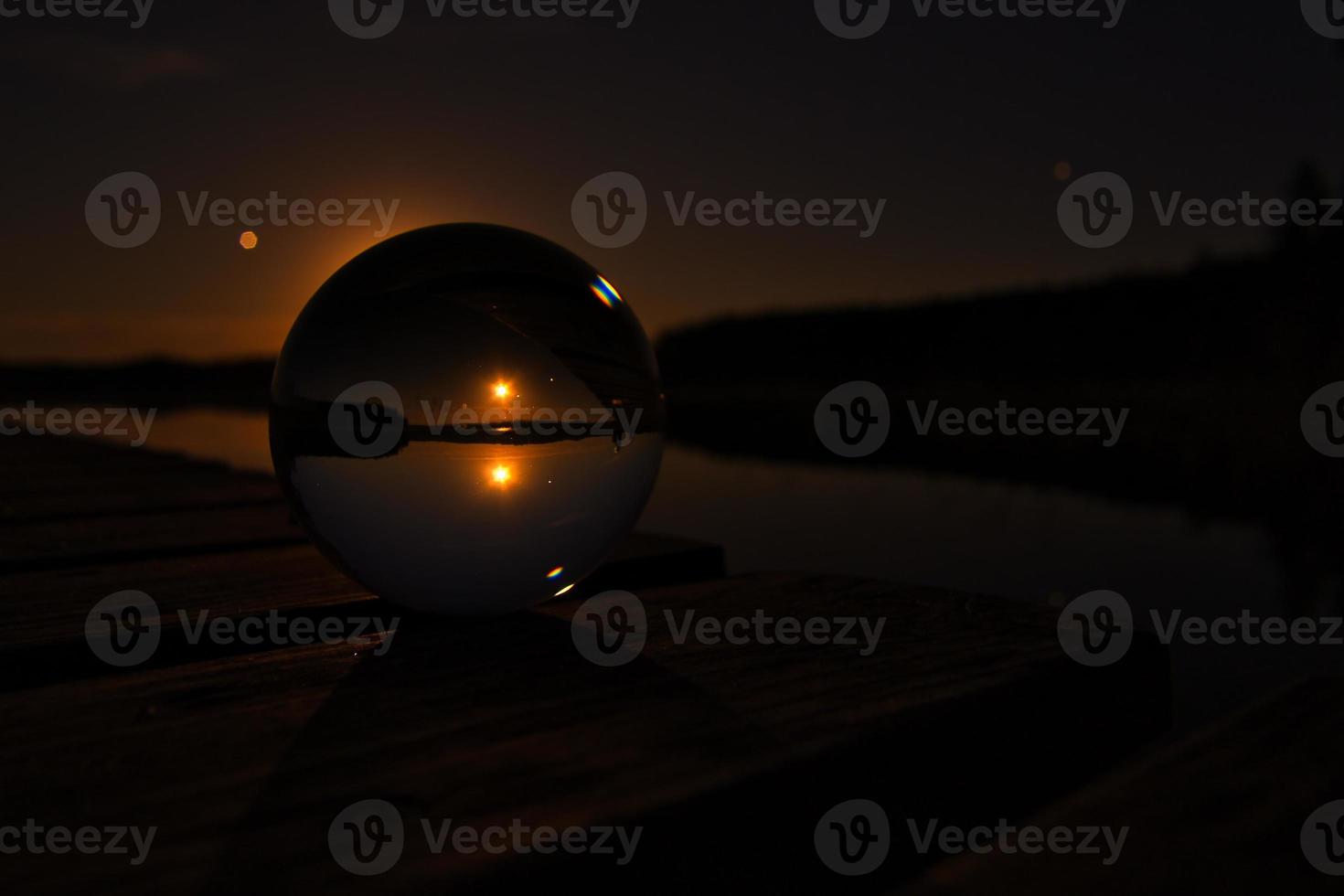 bola de vidro em um cais de madeira em um lago sueco à noite. estrelas e lua foto