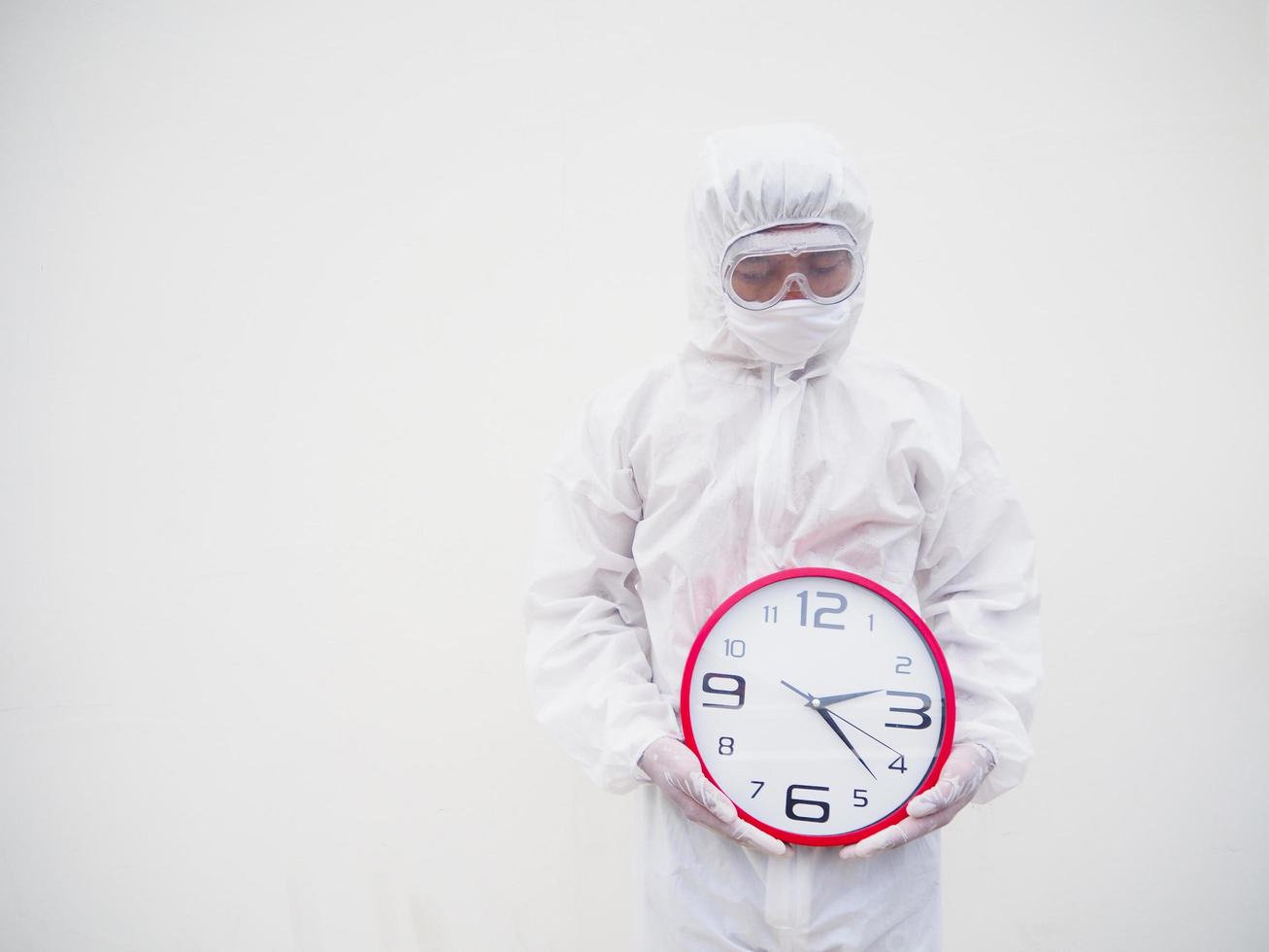 retrato de médico ou cientista em uniforme de suíte de ppe segurando o despertador vermelho e olhando para baixo em vários gestos. fundo branco isolado conceito covid-19 foto