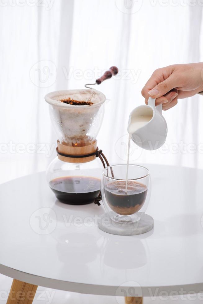 homem derramando leite em copo com café frio na mesa foto
