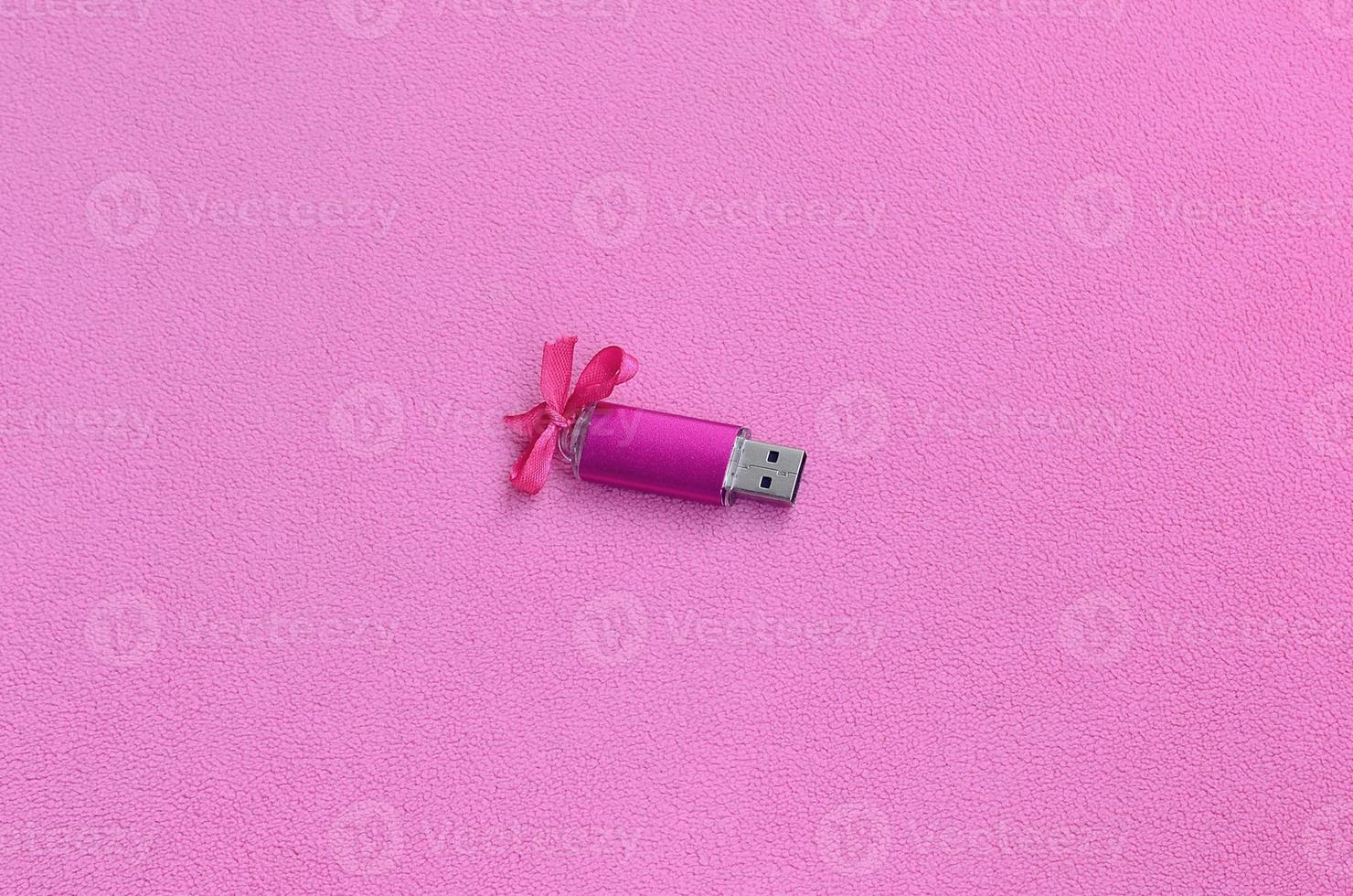 cartão de memória flash usb rosa brilhante com um laço rosa encontra-se em um cobertor de tecido de lã rosa claro macio e peludo. design de presente feminino clássico para um cartão de memória foto