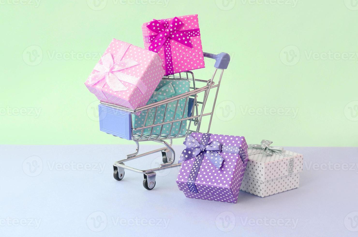 pequenas caixas de presente de cores diferentes com fitas no carrinho de compras em um fundo pastel violeta e azul foto
